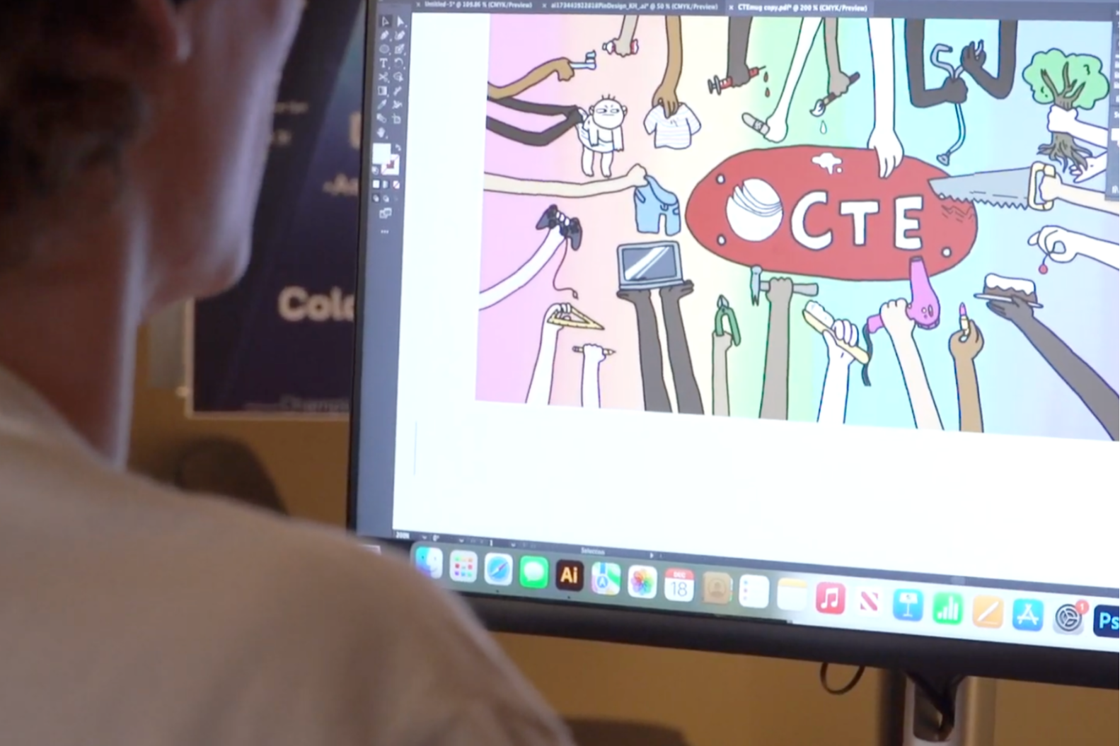 Person watches a computer monitor displaying a colorful illustration with objects and a red logo.
