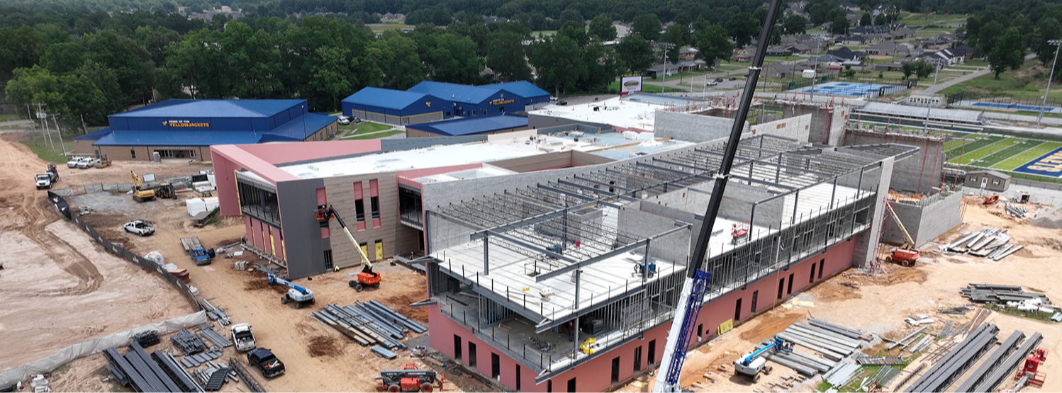 Aerial view of a construction site featuring an unfinished building, machinery, and construction materials on a cloudy day.