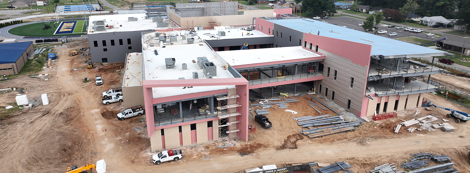 Aerial view of a construction site with an unfinished building and various machinery vehicles on a dirt ground.