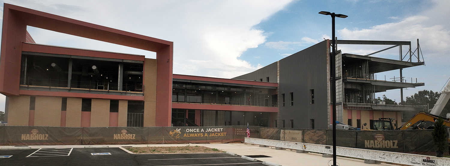 A large building under construction with a modern architectural design. The building has a red and gray exterior.