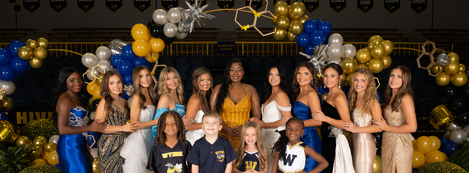 A group of people, including young children, pose for a photo in front of balloons on a basketball court.