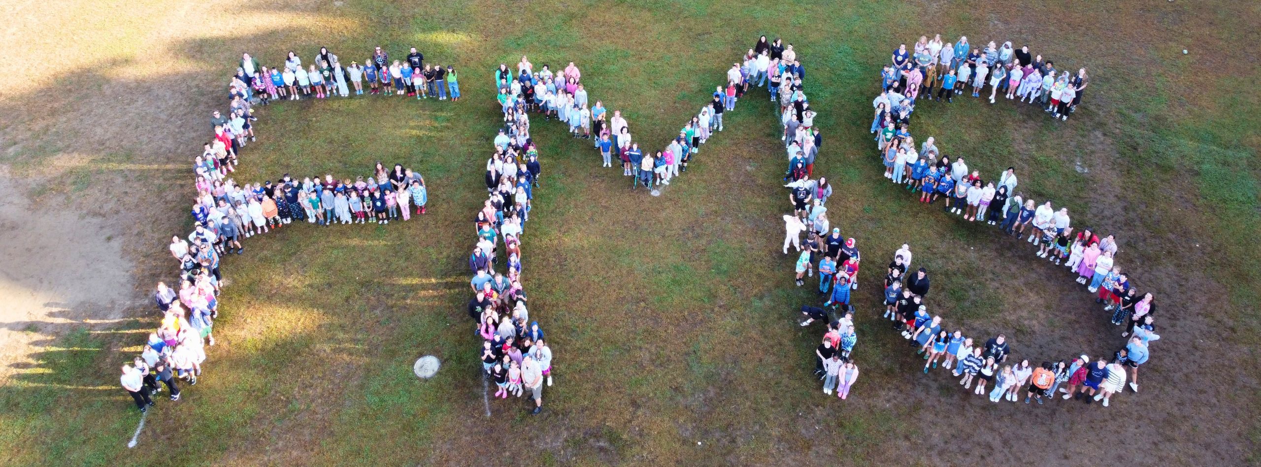 An aerial view of a group forming the letters FMS on a grassy field.