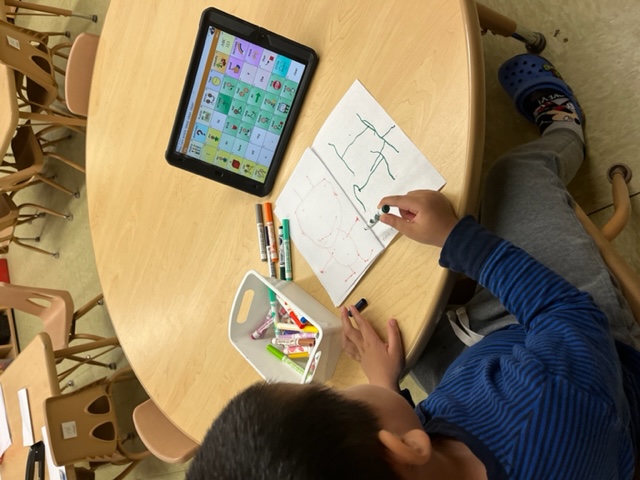 A children writes at a table while referencing an iPad