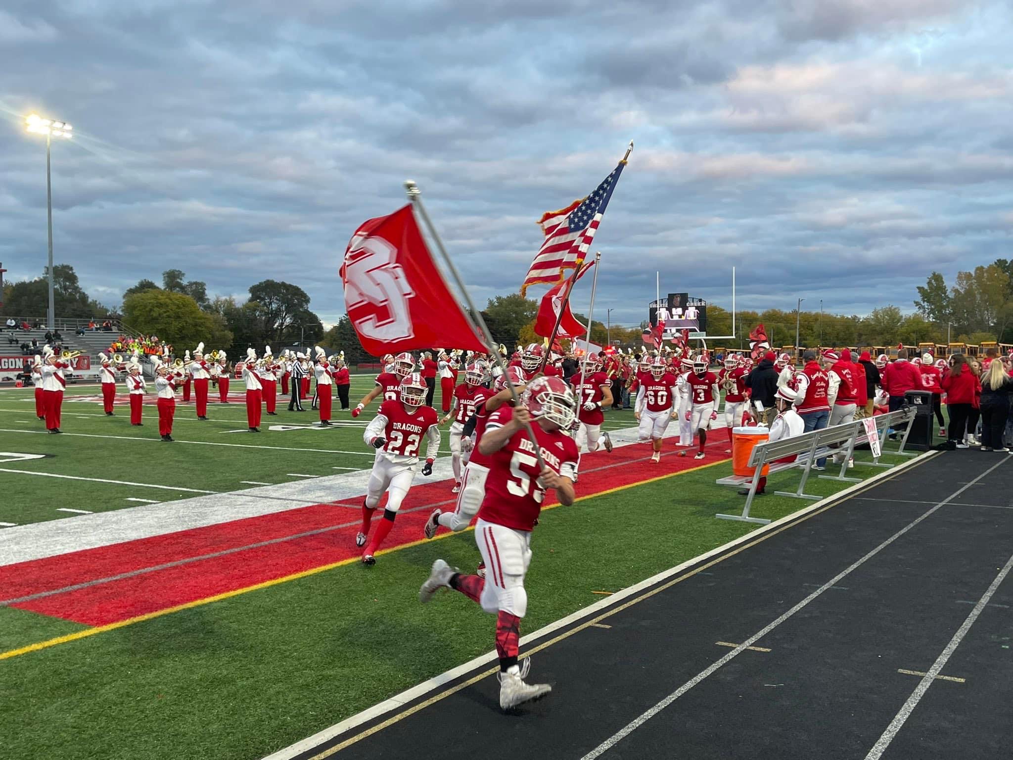 Varsity football players running on the field with SC flags