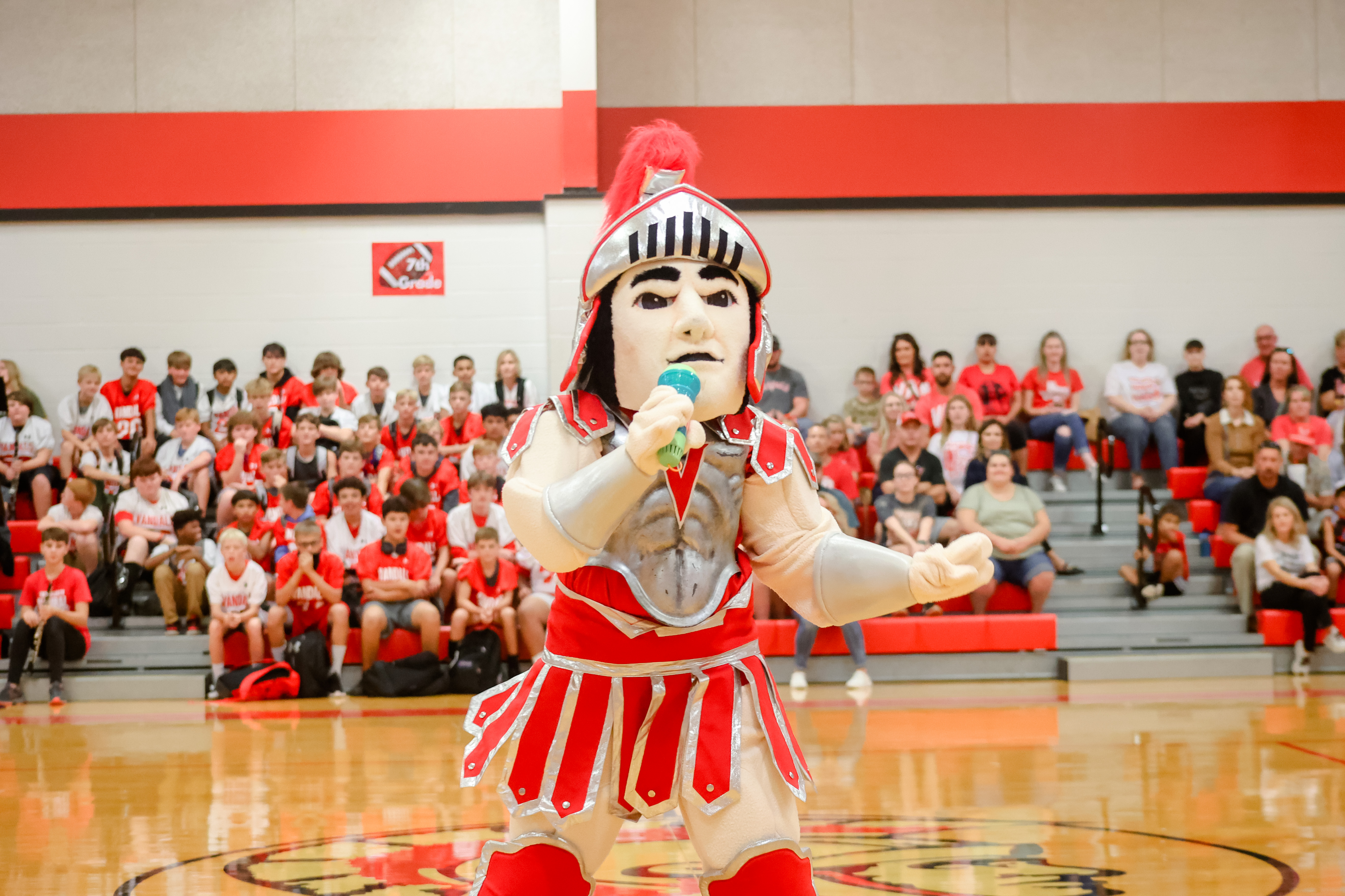 mascot sings into microphone in front of the crowd at a pep rally