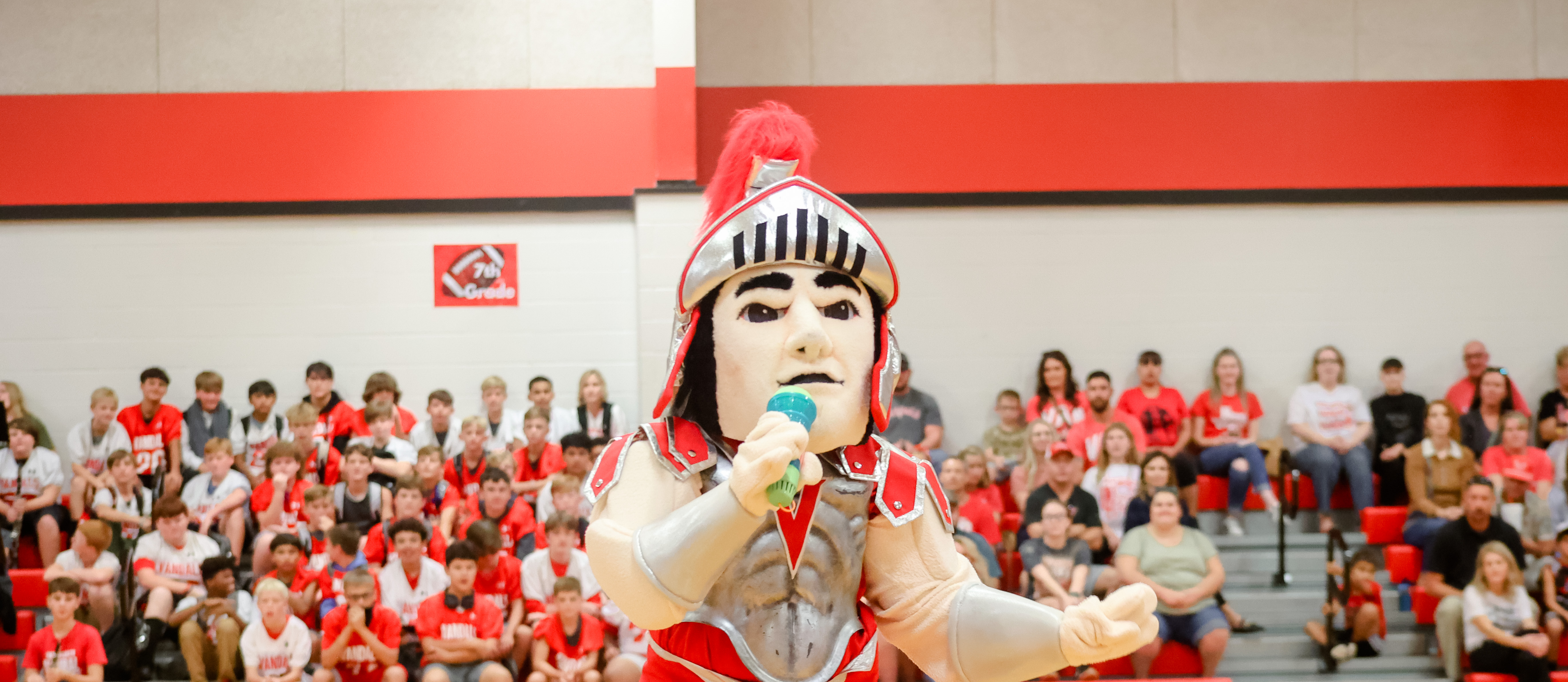 mascot sings into microphone in front of the crowd at a pep rally