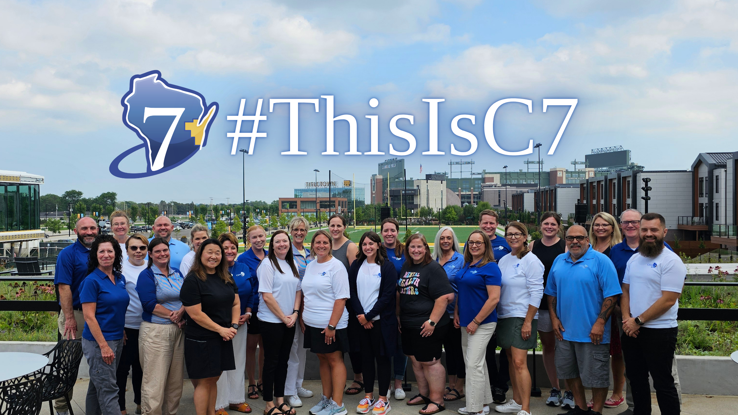 CESA 7 staff members standing in a group with Lambeau Field in the background.  CESA 7 logo and #ThisIsC7