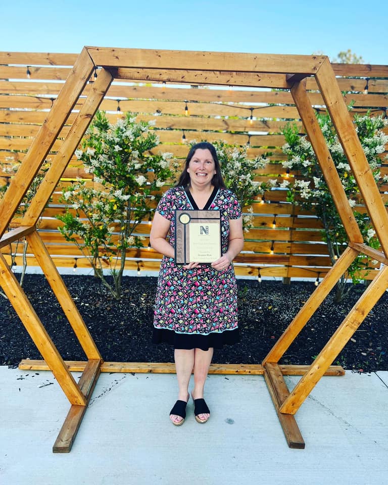Mrs. Hale standing inside a wooden frame holding a certificate