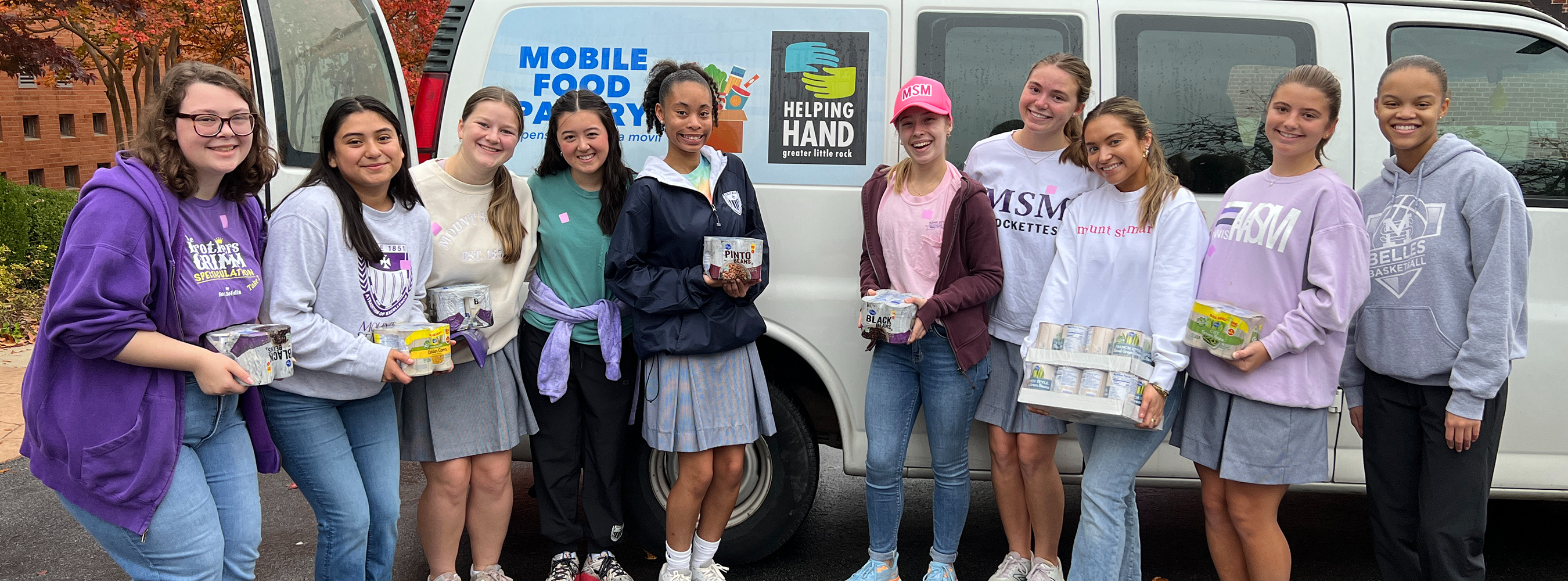 students holding donated canned food items in front of Mobile Food Pantry van