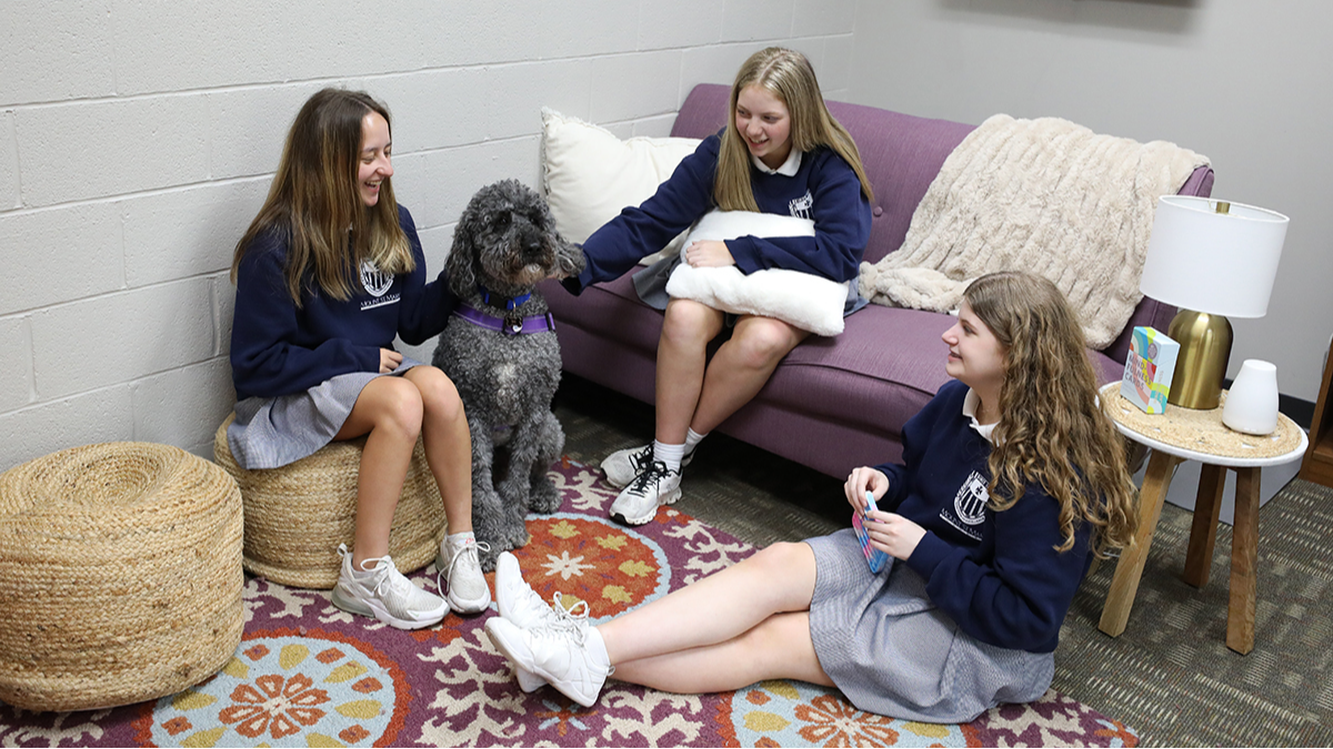 three students gathered in Wellness Center with a therapy dog