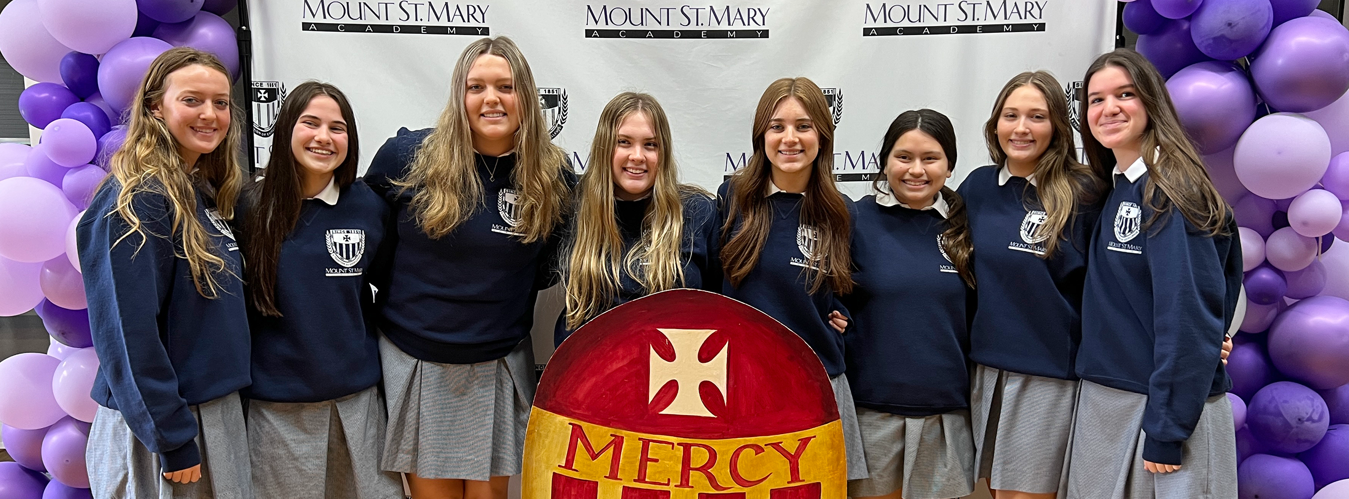 group of students standing with sign of Mercy shield