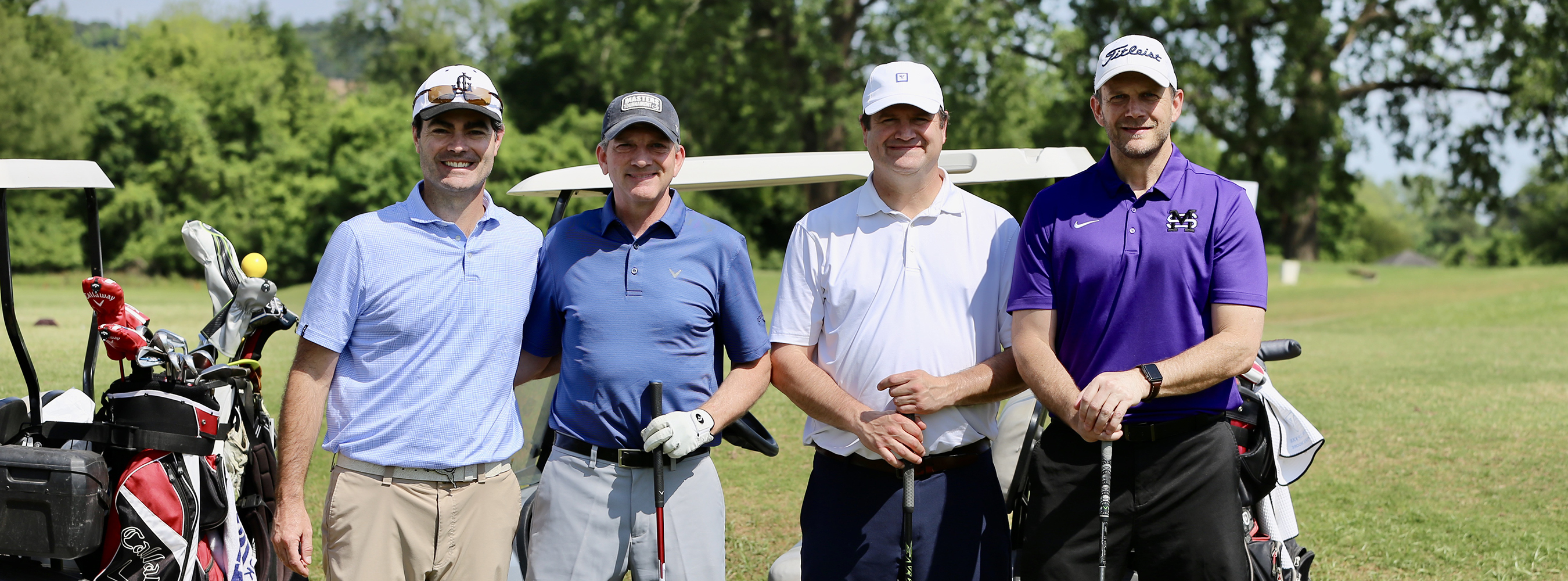 four golfers standing with golf clubs near golf course