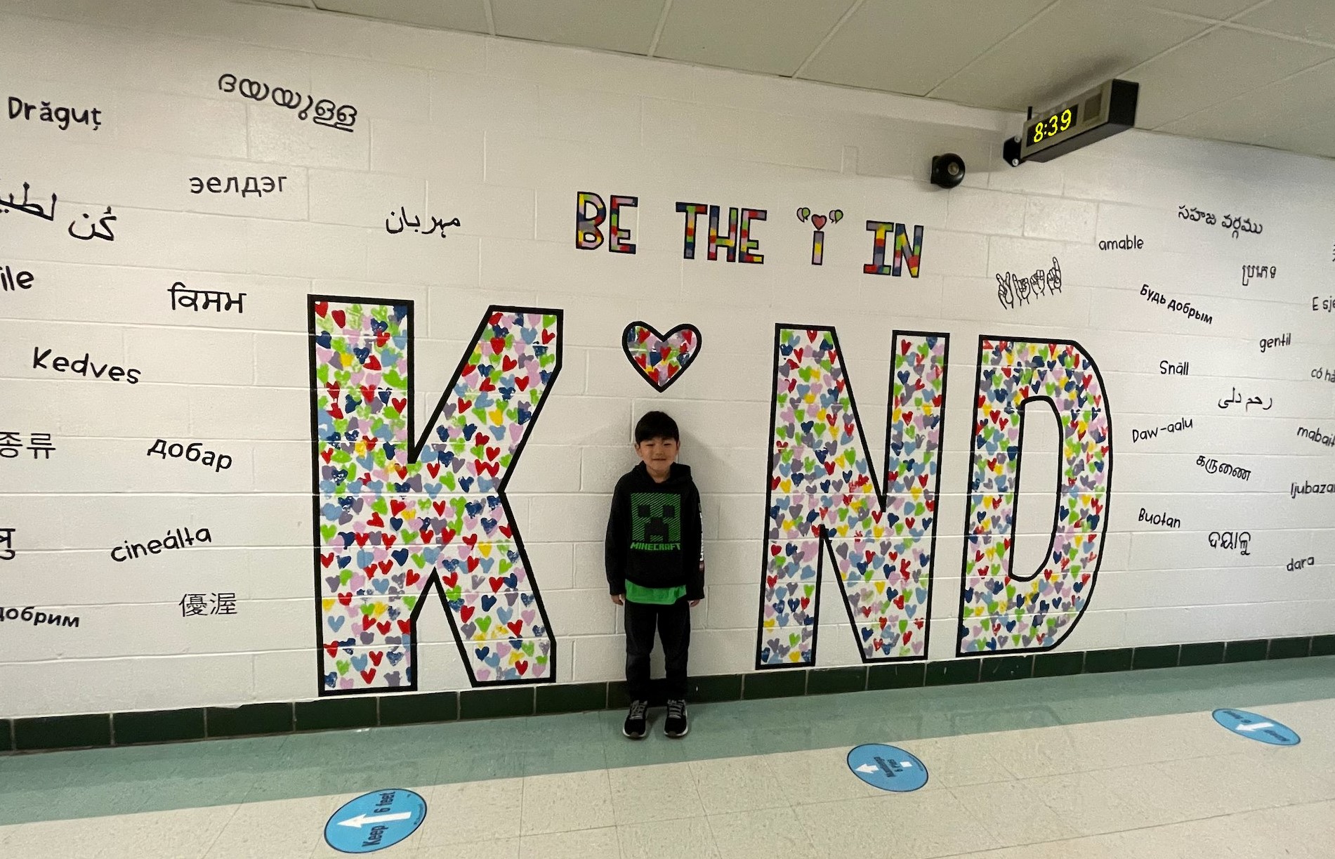 A child stands in front of an art mural that spells out the word KIND