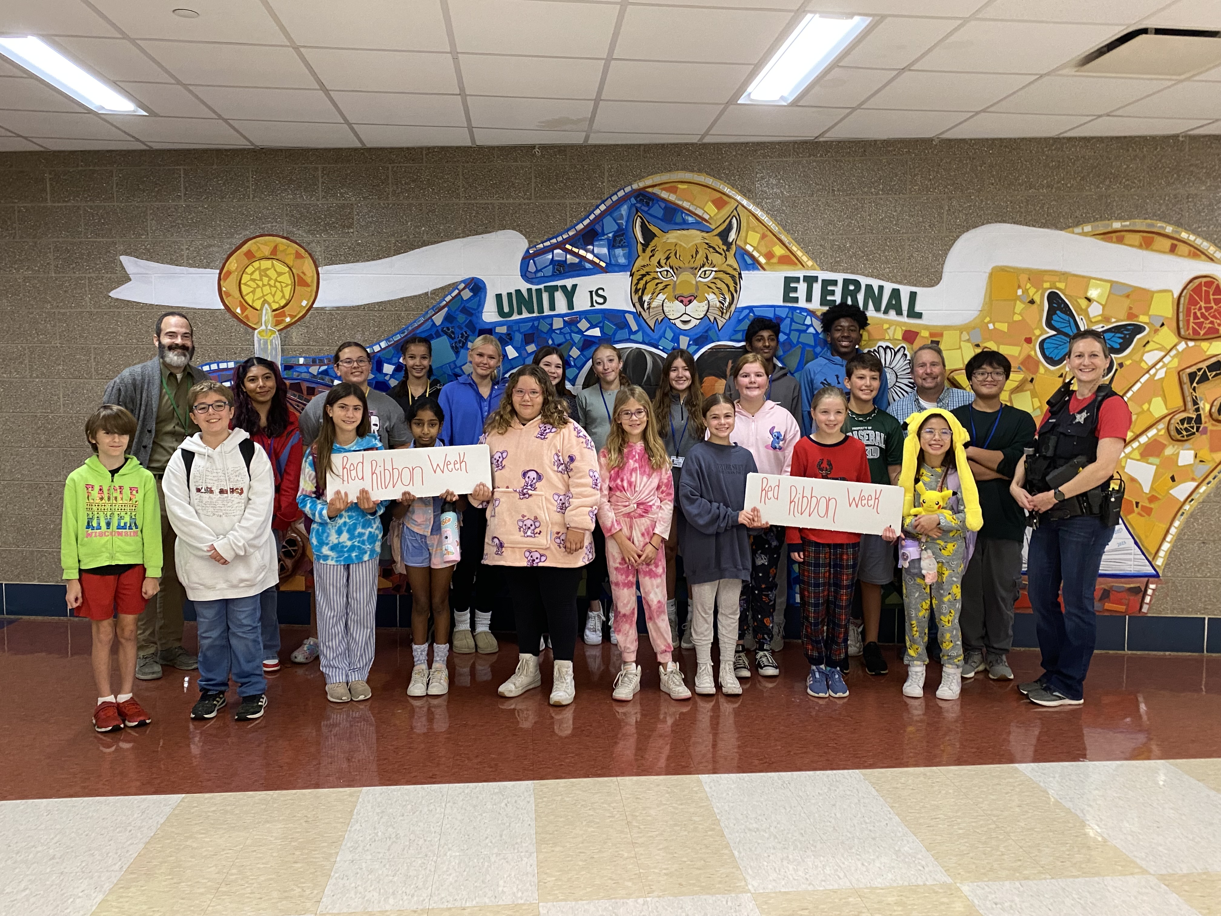 A large group of students stands in front of a mural with "Red Ribbon Week" signs