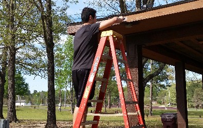 A student on a ladder helping build a pavilion in the park