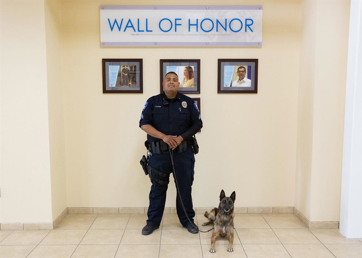 Officer Edward and Uma in front of the Wall of Honor sign