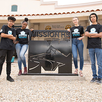 four students smiling around the Mission High School sign in front of the building