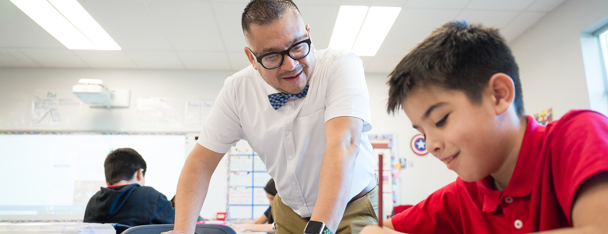 Teacher standing next to a student assisting with an assignment