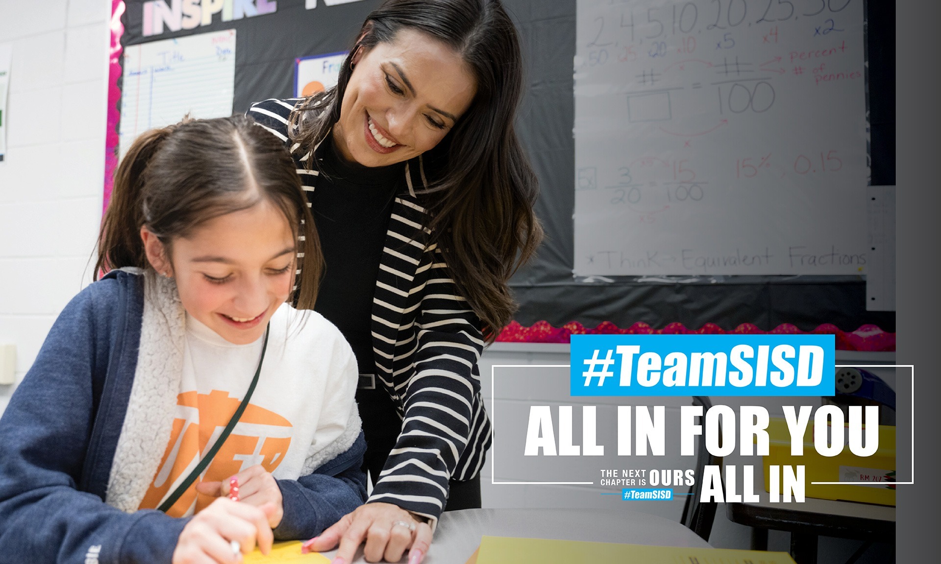 SISD teacher assisting an SISD student in the classroom both of them smiling, next to #TeamSISD All in for You