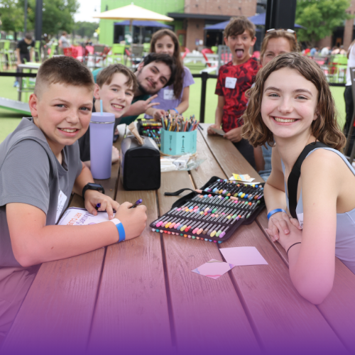 Group of students at a table coloring and smiling at the camera