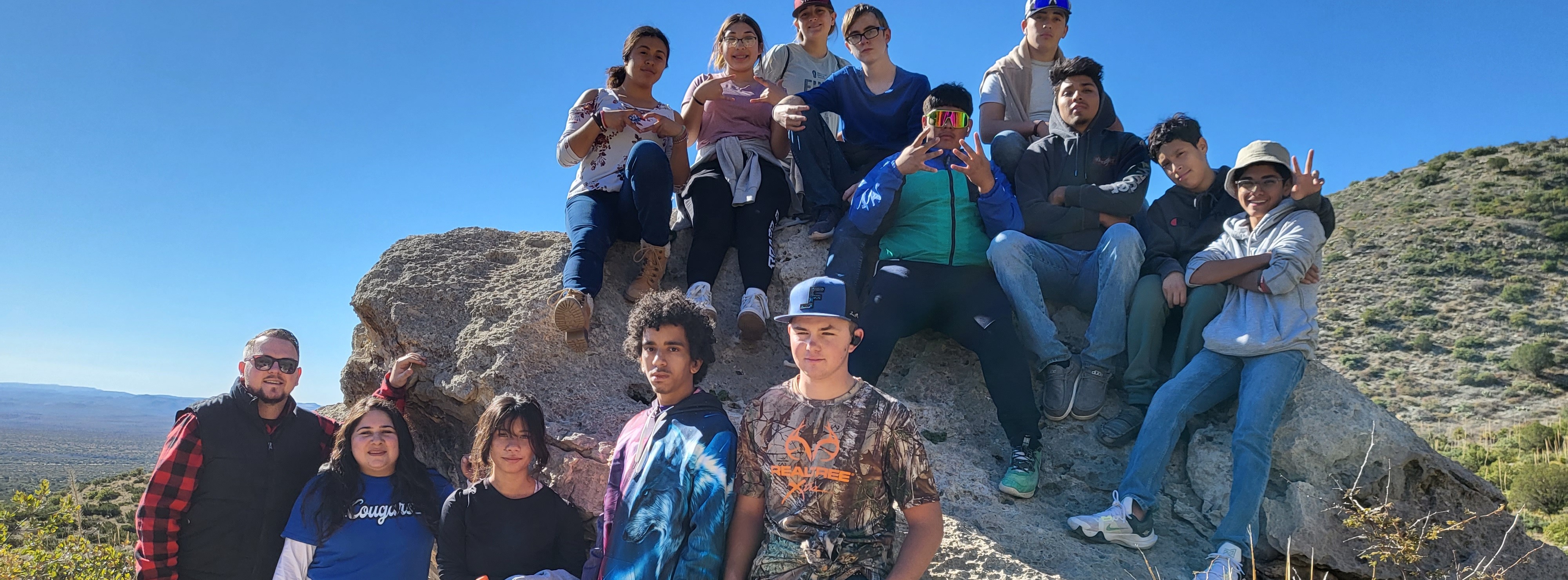 Students posing on a large rock while out in the wilderness on a trip