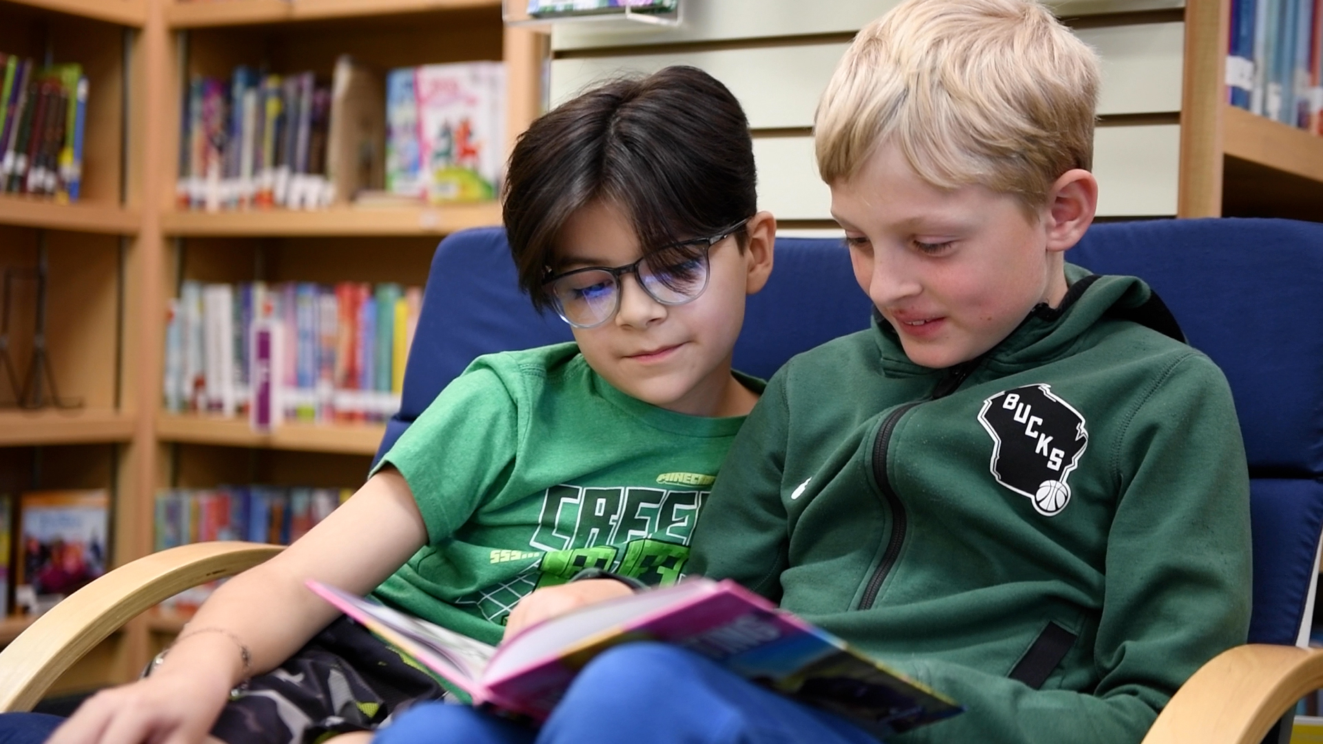 two students reading a book together in the library