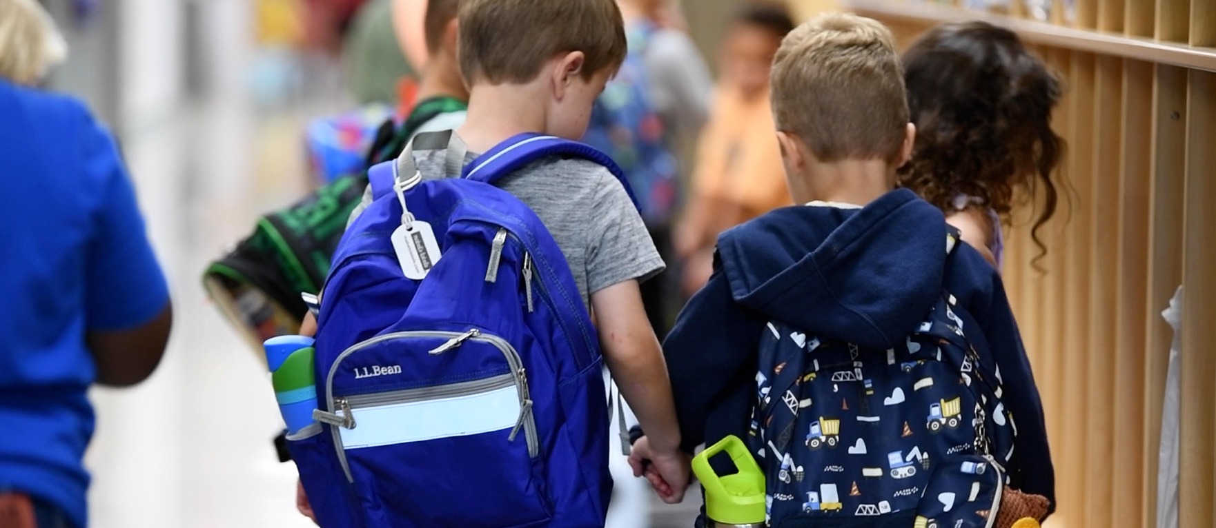two students with backpacks on holding hands walking down the school hallway