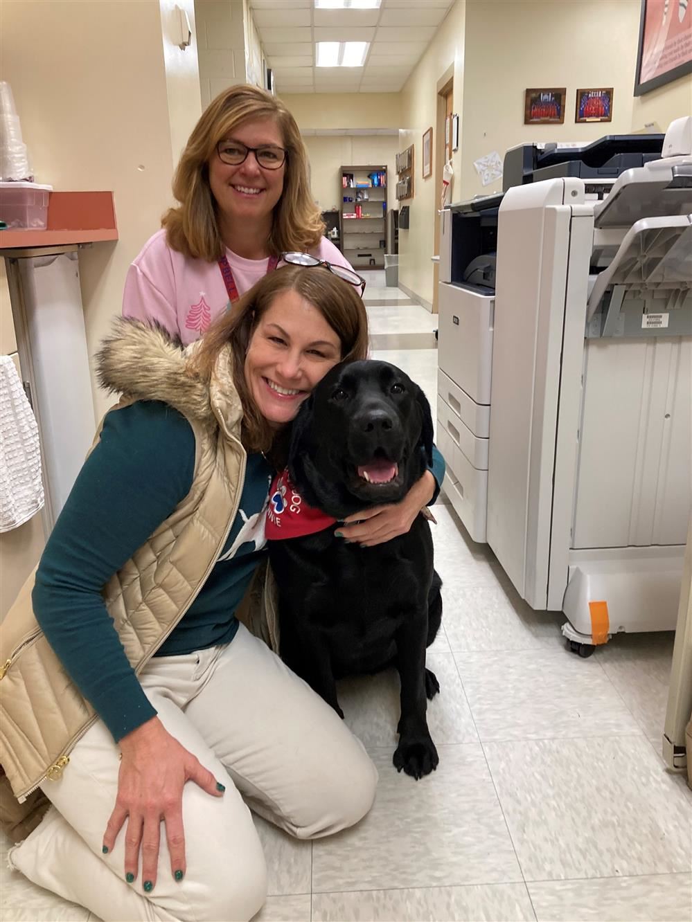 Two counselors smile with black Labrador retriever wearing support animal vest
