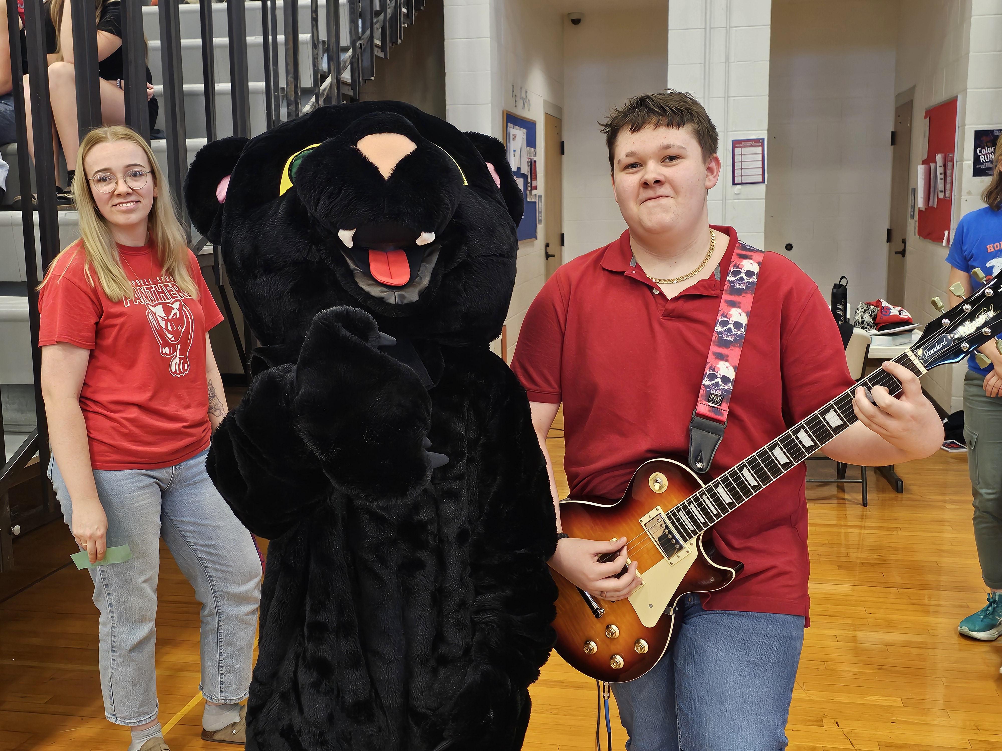 STudent holding guitar while standing next to school panther mascot