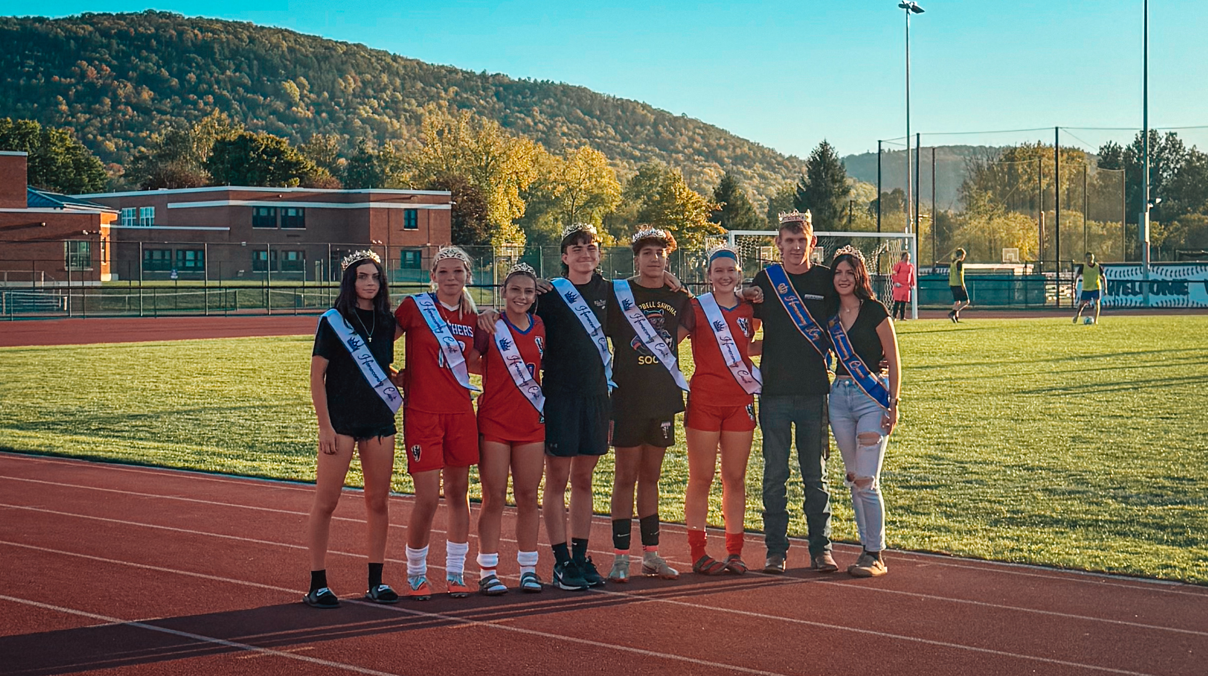 Homecoming court posing outside on the track with sashes