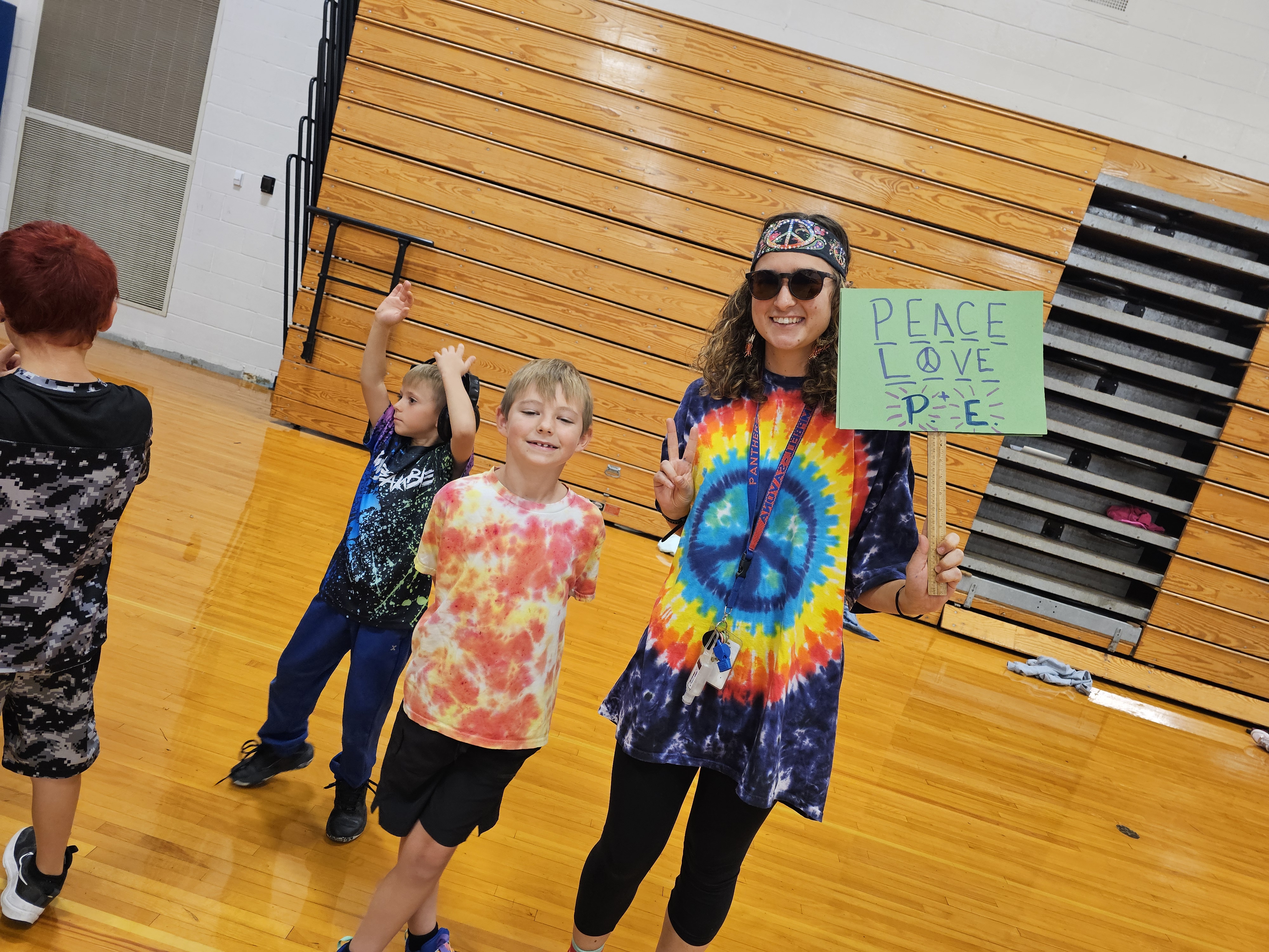 STudent and teacher dressed in tie die holding a peace sign in the gym