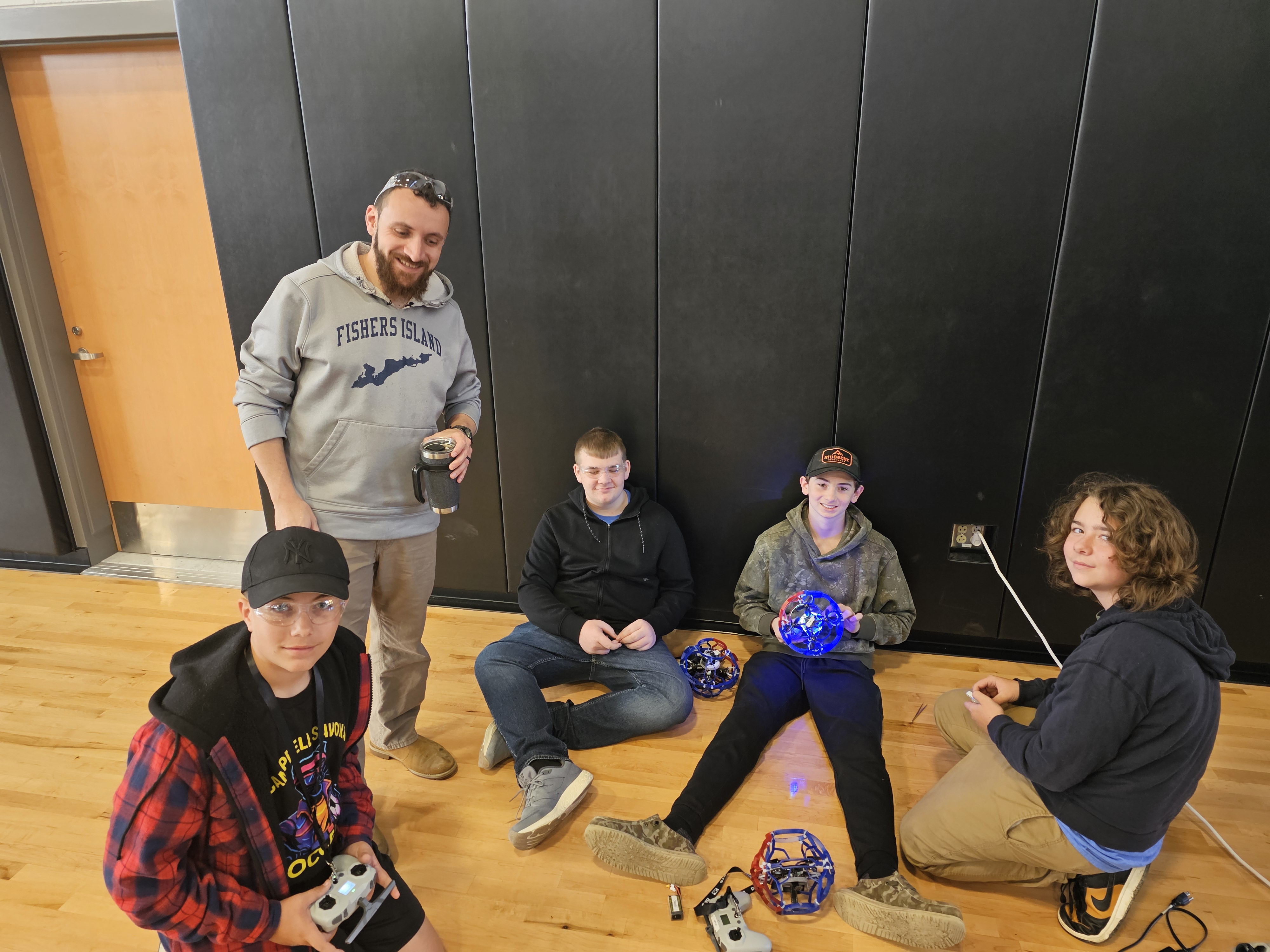 Coach with 4 students sitting on gym floor working on drones