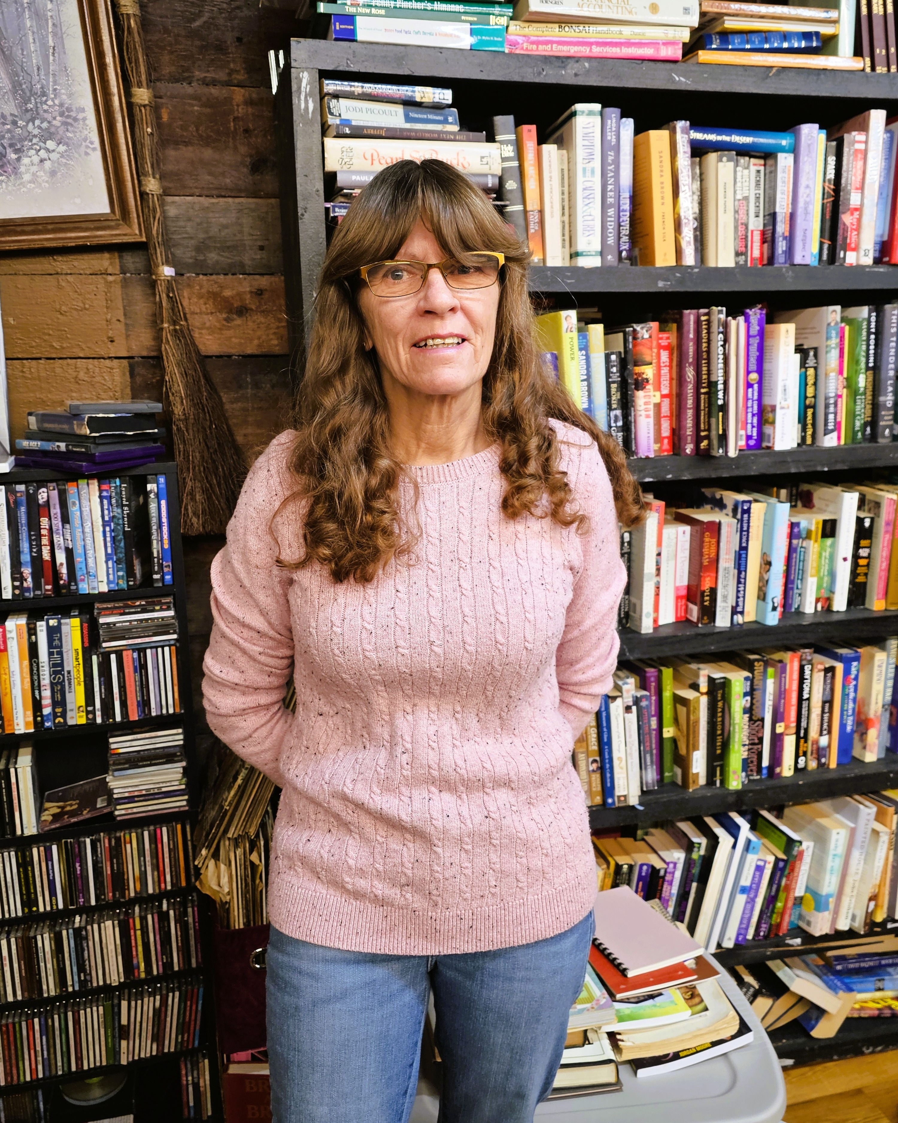 Person with pink sweater and jeans standing in front of a bookshelf