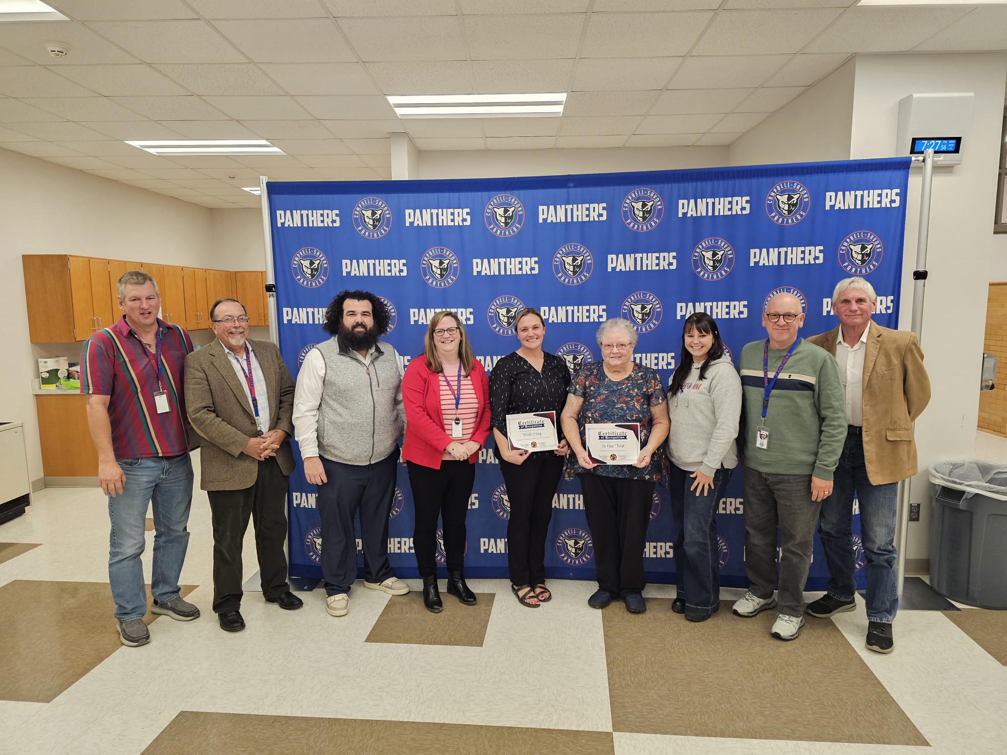 BOE Group picture in front of banner celebrating community member and teacher