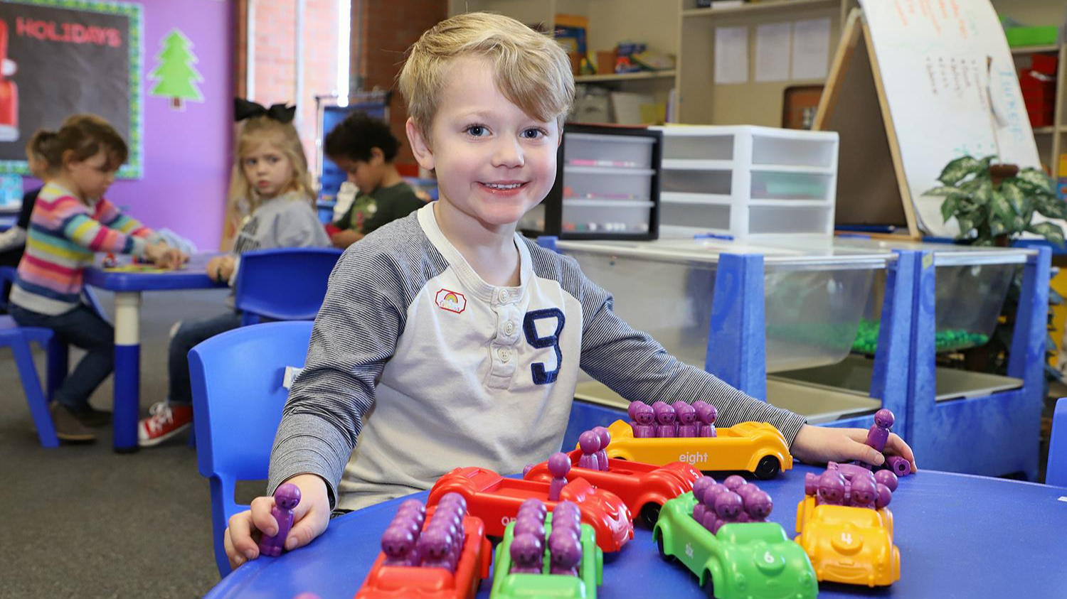 Little boy smiling while learning with manipulatives. Manipulatives of cars and people. 