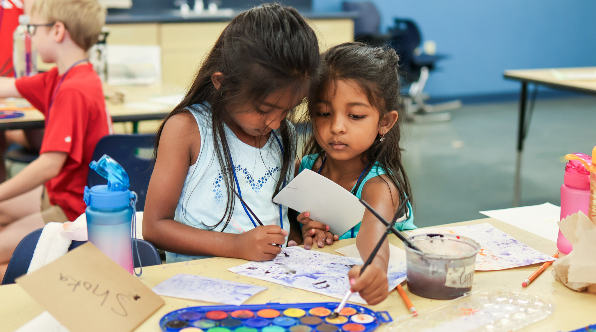 two girls work on a craft at a table