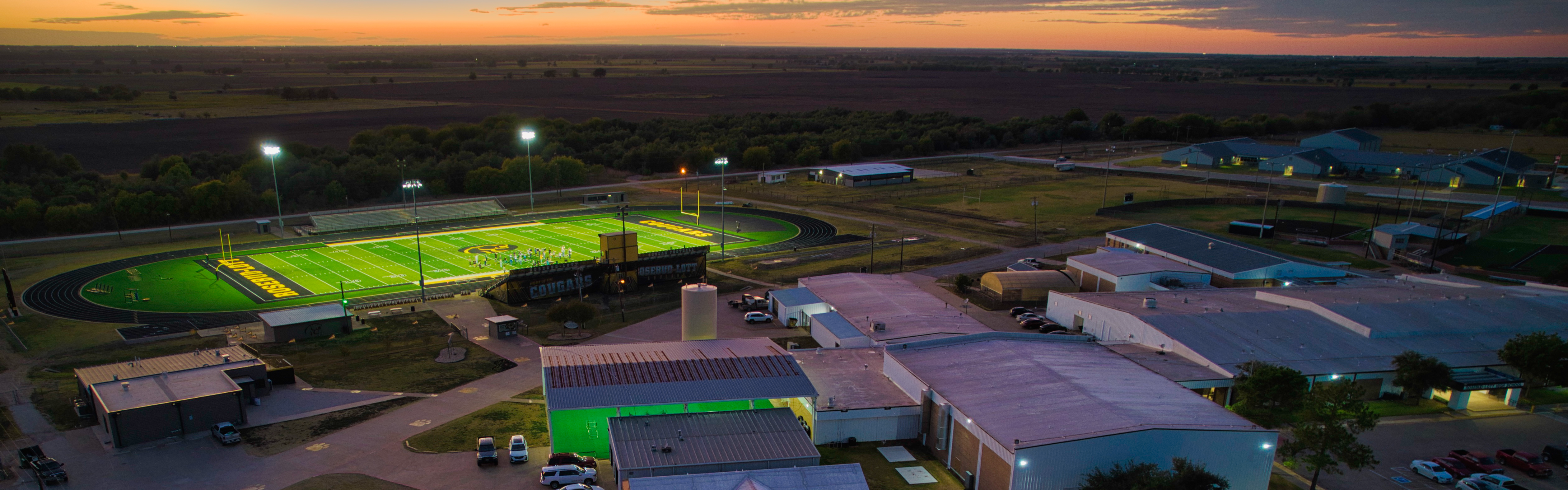 Aerial photo of campus buildings and football field in the evening