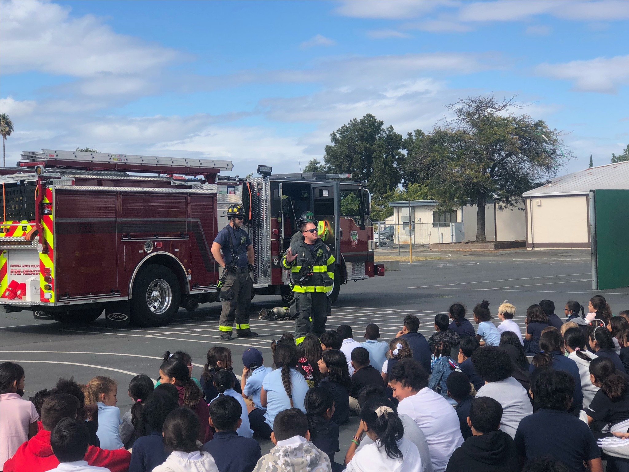 Students outside with firemen presenting information. 
