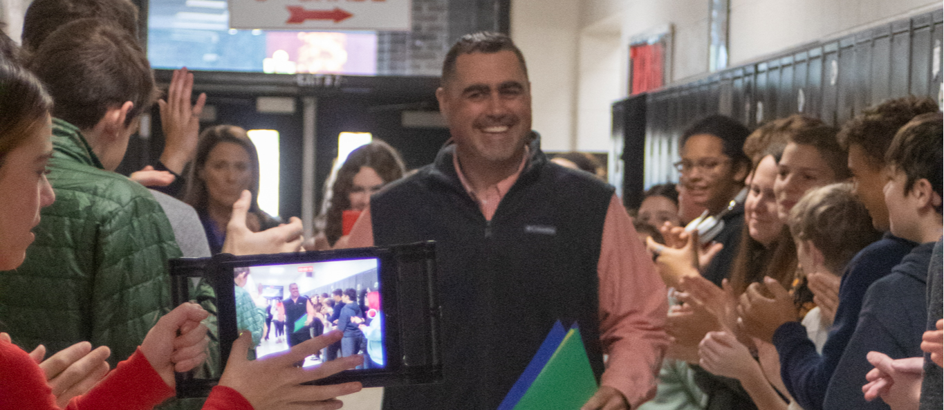 A principal walks down a hall of students lined against the walls.