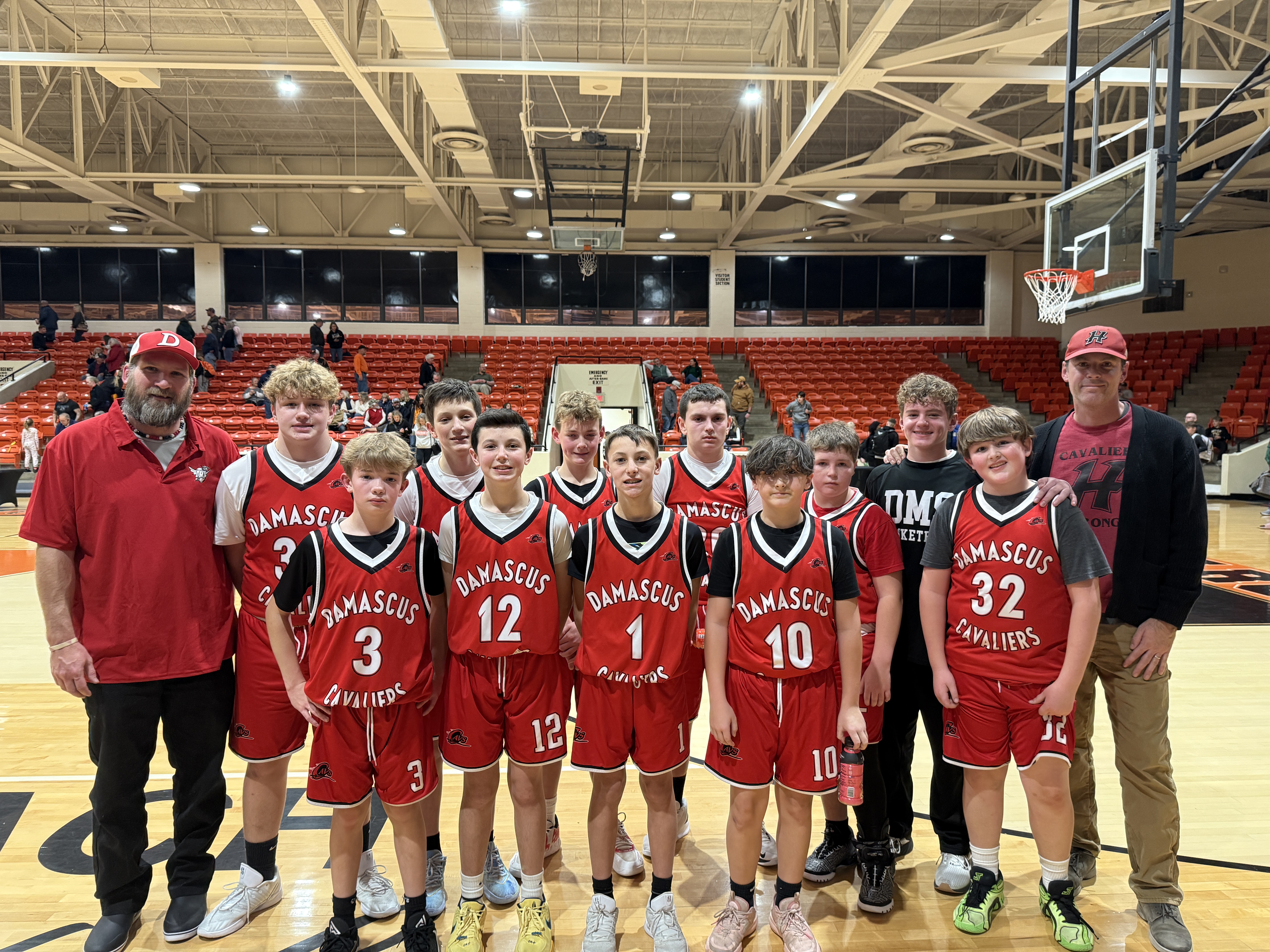 A boys basketball team poses with their coaches in a gym.