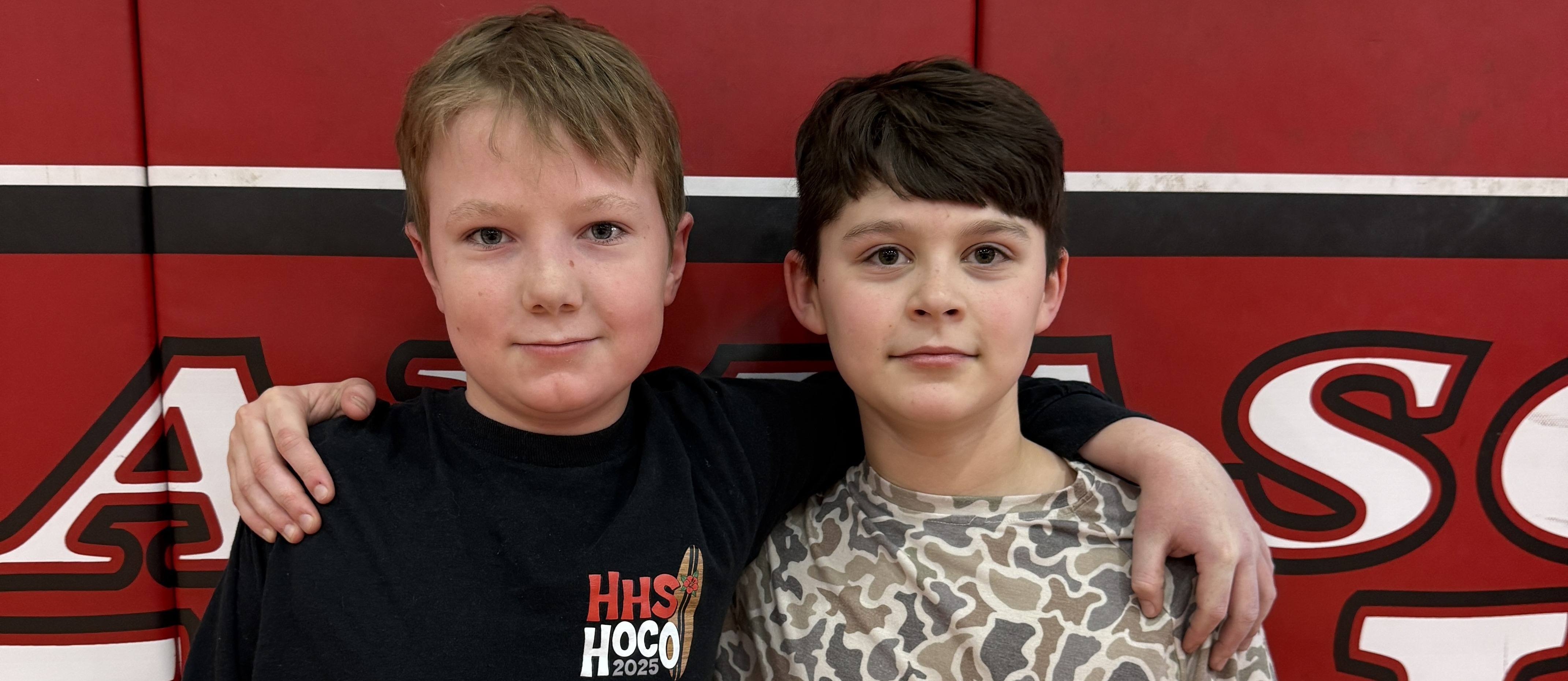 Two students stand in front of a red wall.
