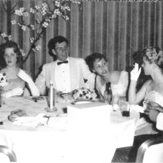 group of guys and girls sitting around a table in suits and dresses