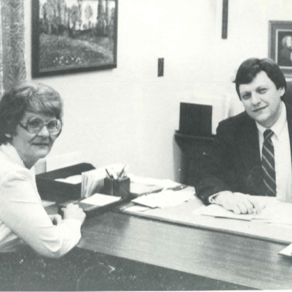 1985 Pete Flaig and Evelyn Fultz sitting at a desk smiling