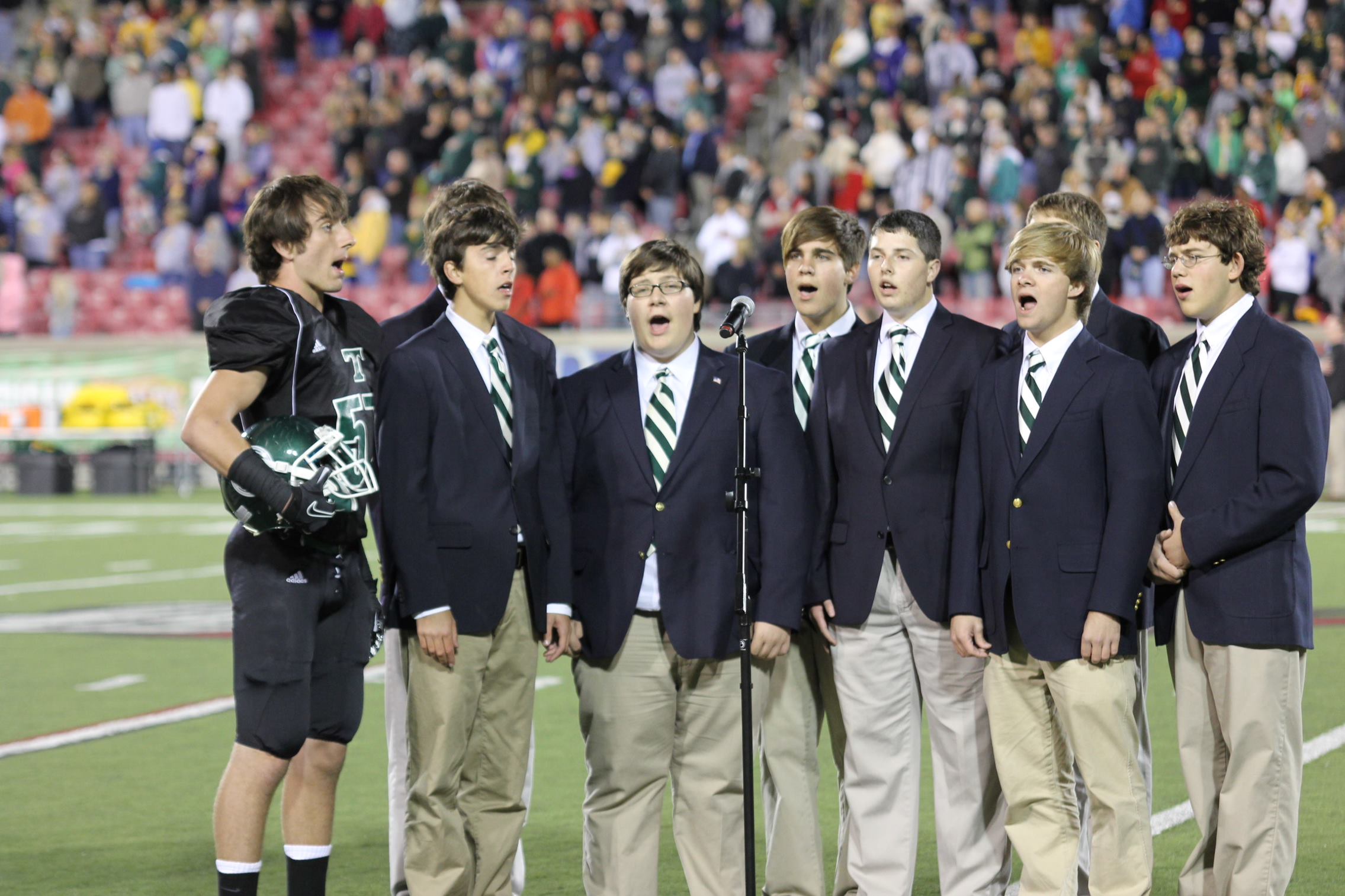 9 people standing and singing on the football field