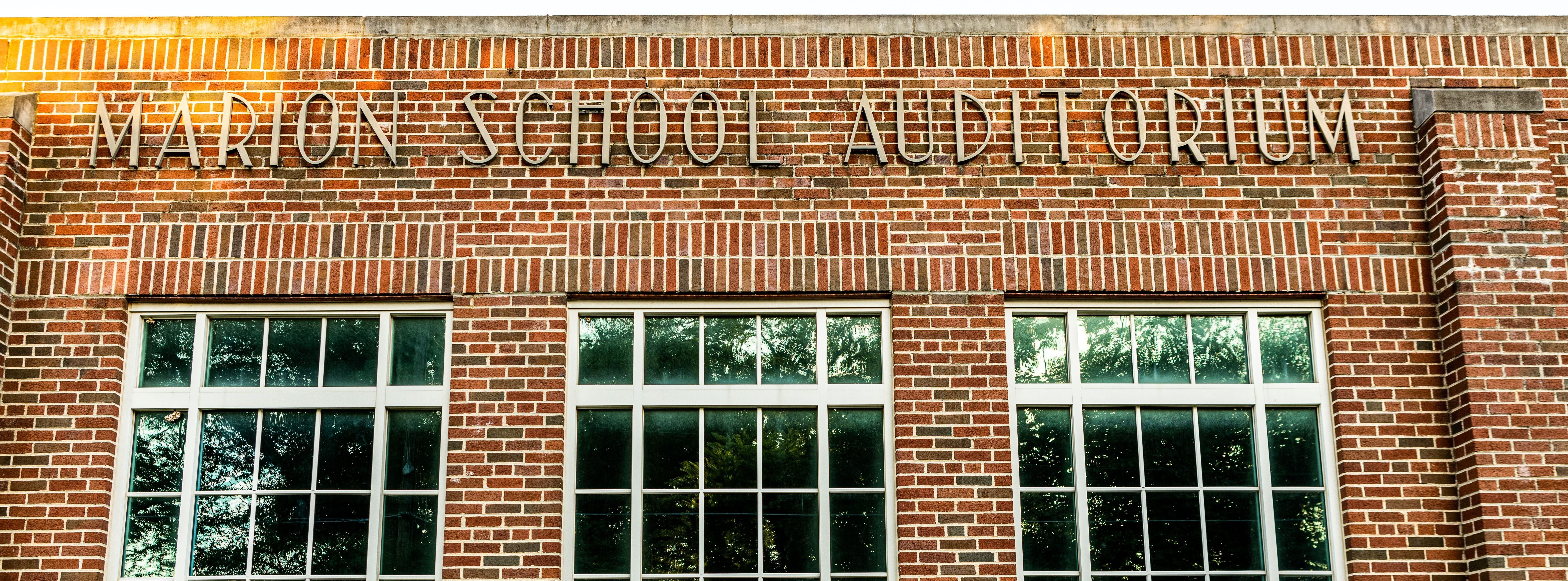 Brick exterior of the Marion School Auditorium building with large windows and the words “Marion School Auditorium” displayed across the top of the façade.