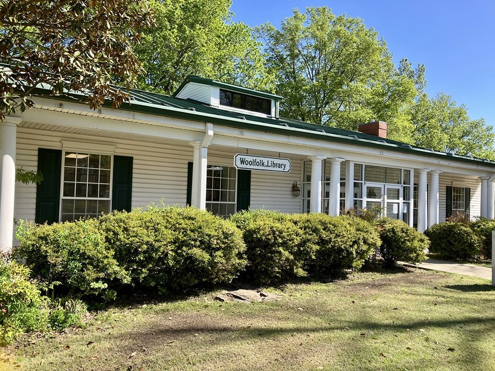 image of the Woolfolk Public Library that is a white house with columns with bushes in the front