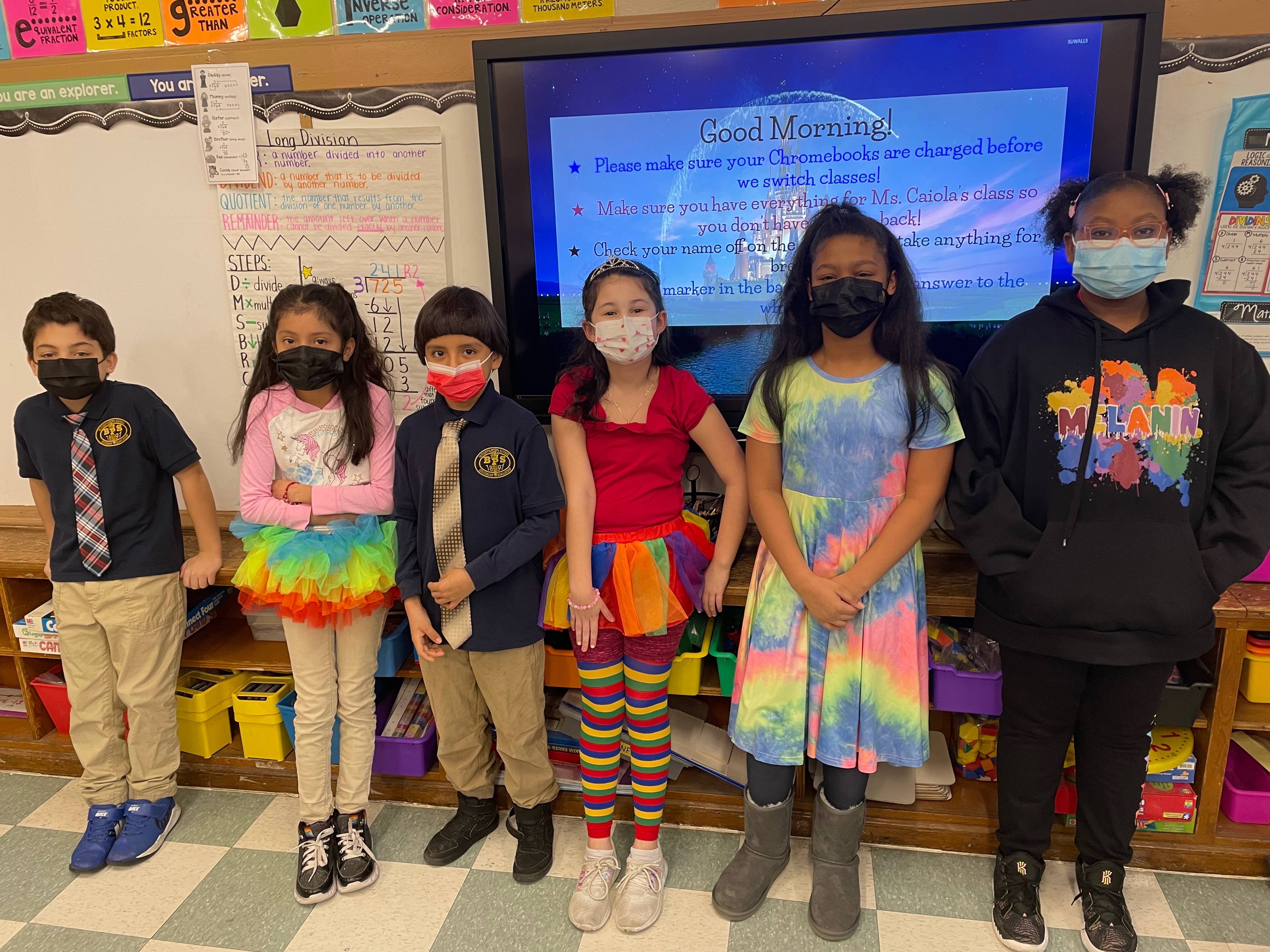 masked students dressed in cheerful colors posing at the front of a classroom