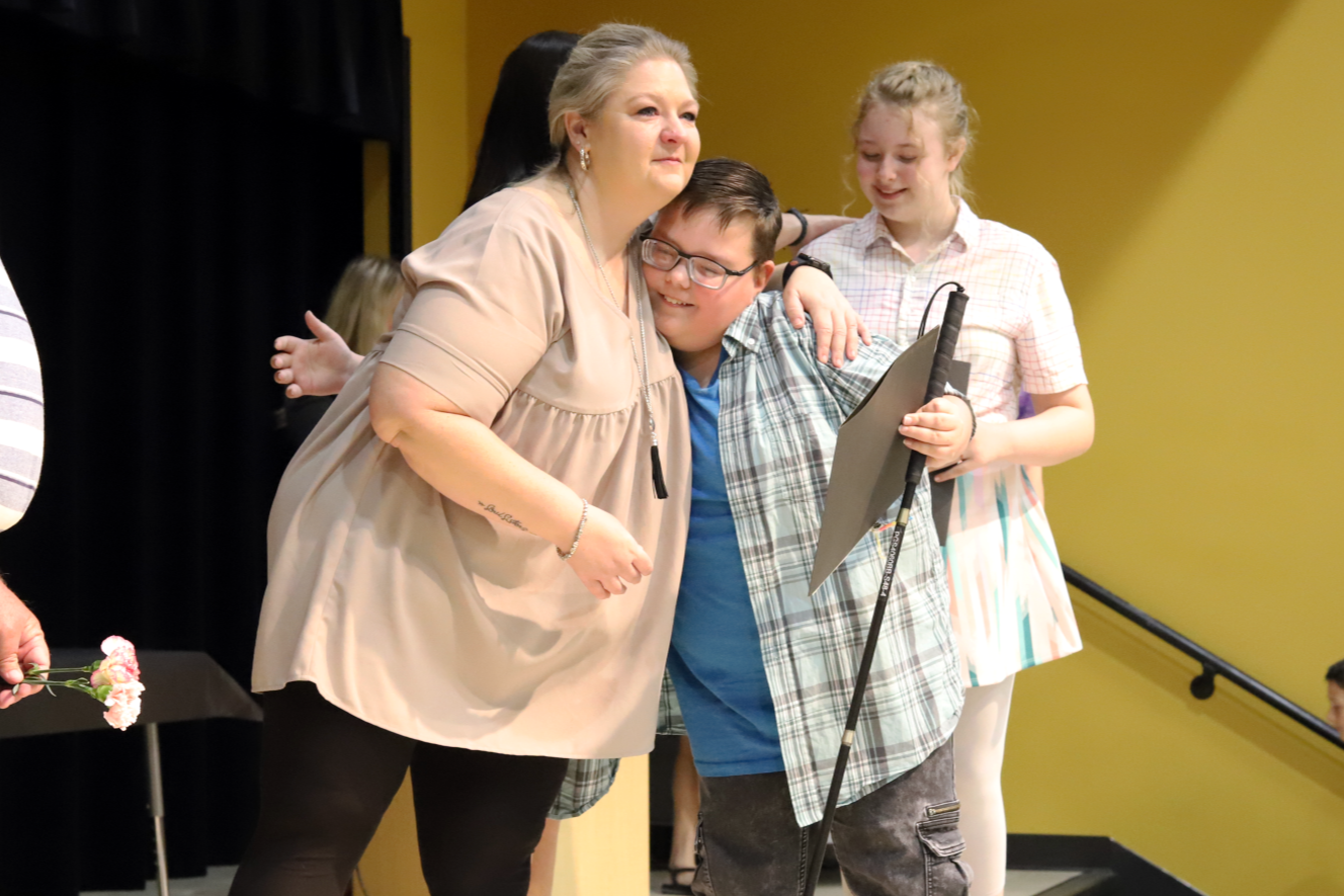 Northwoods counselor hugs student holding a white cane during fifth grade promotion