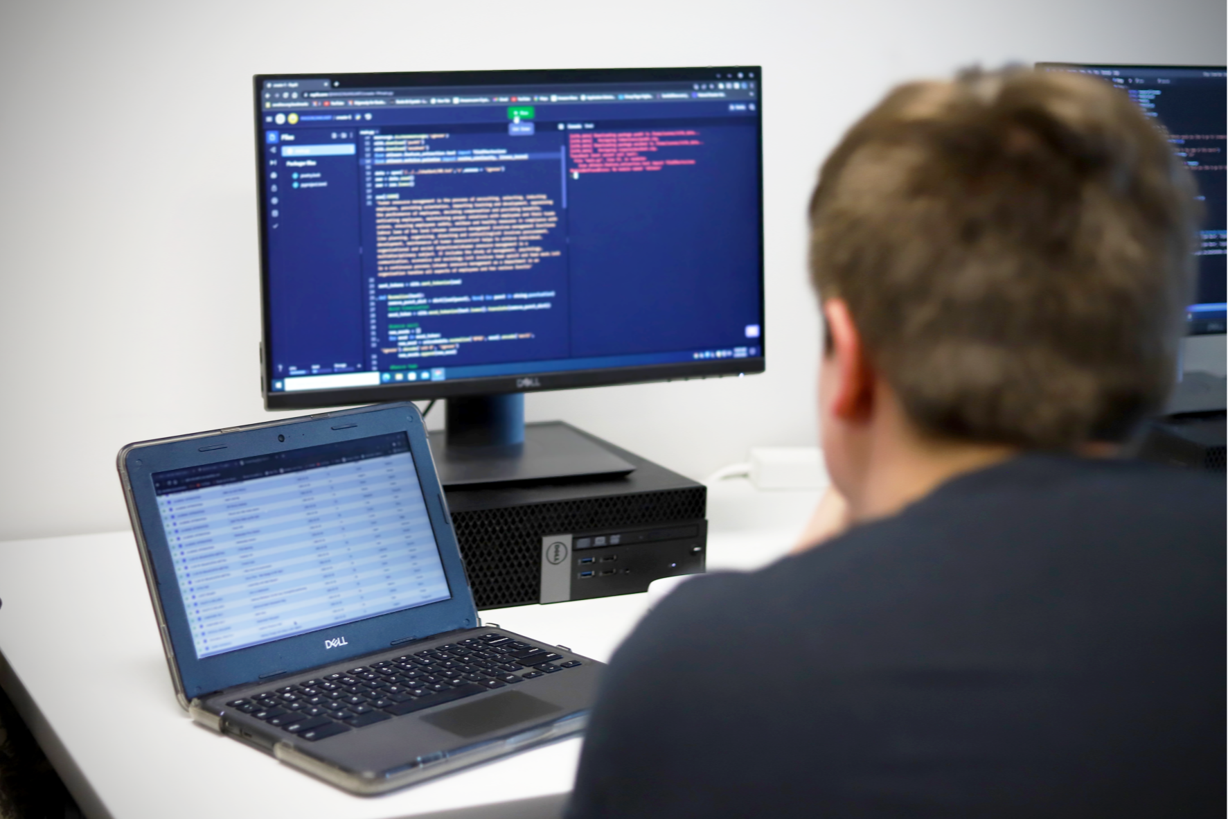 High school computer science student looking at desktop screen and laptop screen displaying programming code