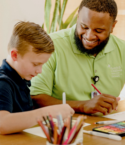 Man in Family & Children's Services polo smiling and drawing with student